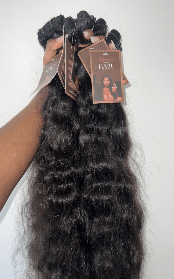 A hand holding a bunch of curly raw Indian hair, showcasing the tight curls, natural texture, and volume of the hair.